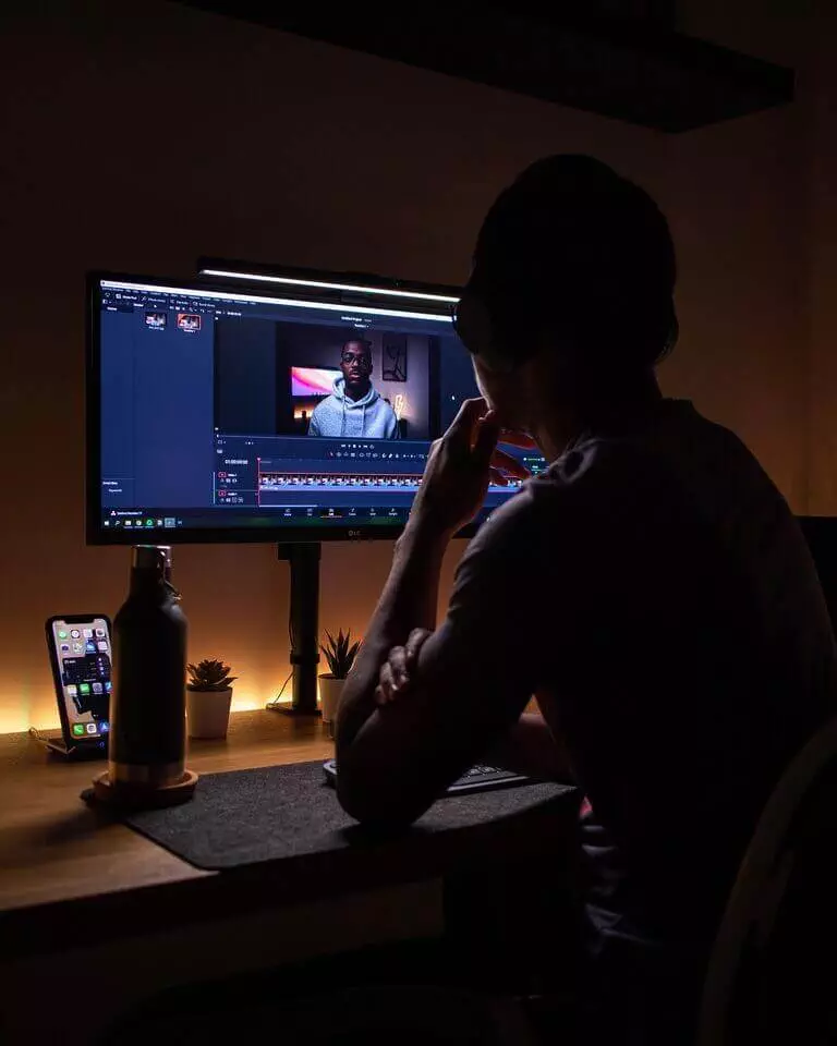 A Man Earning Money As A Youtube Blogger At His Desk With Two Monitors.