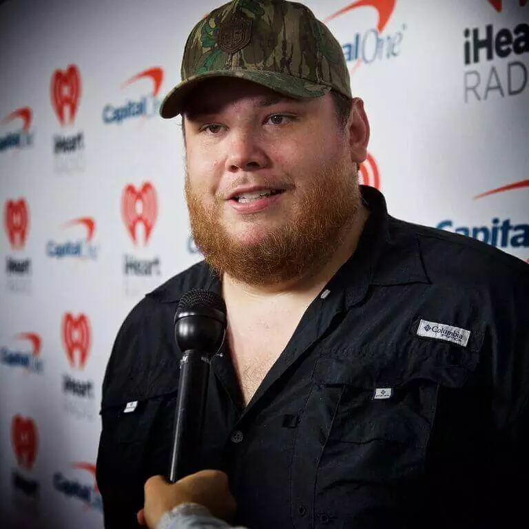 A Bearded Man In A Hat Is Holding A Microphone At Luke Combs